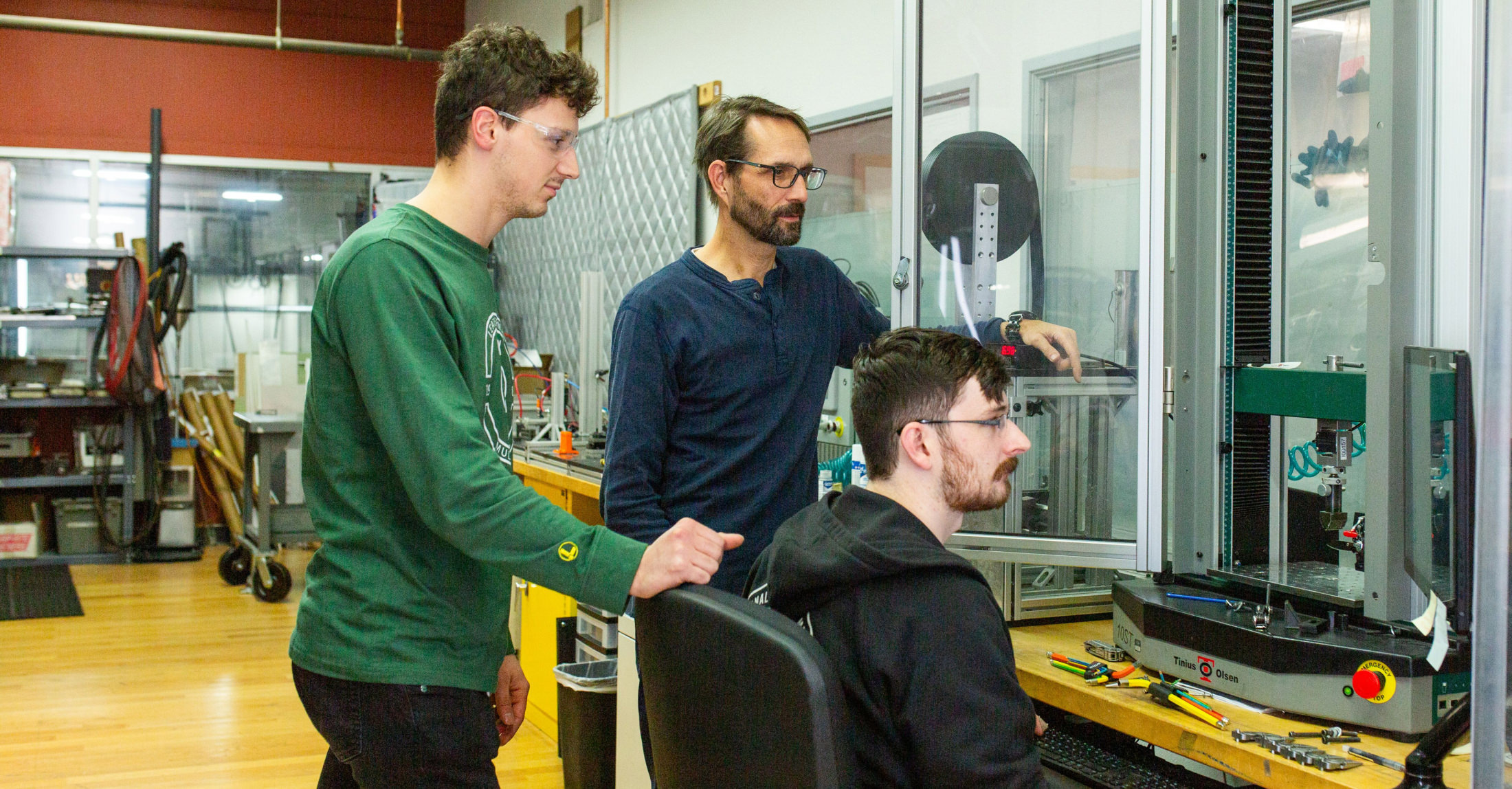 three men collaborating on a machine in a factory setting, focused on their task and surrounded by industrial equipment