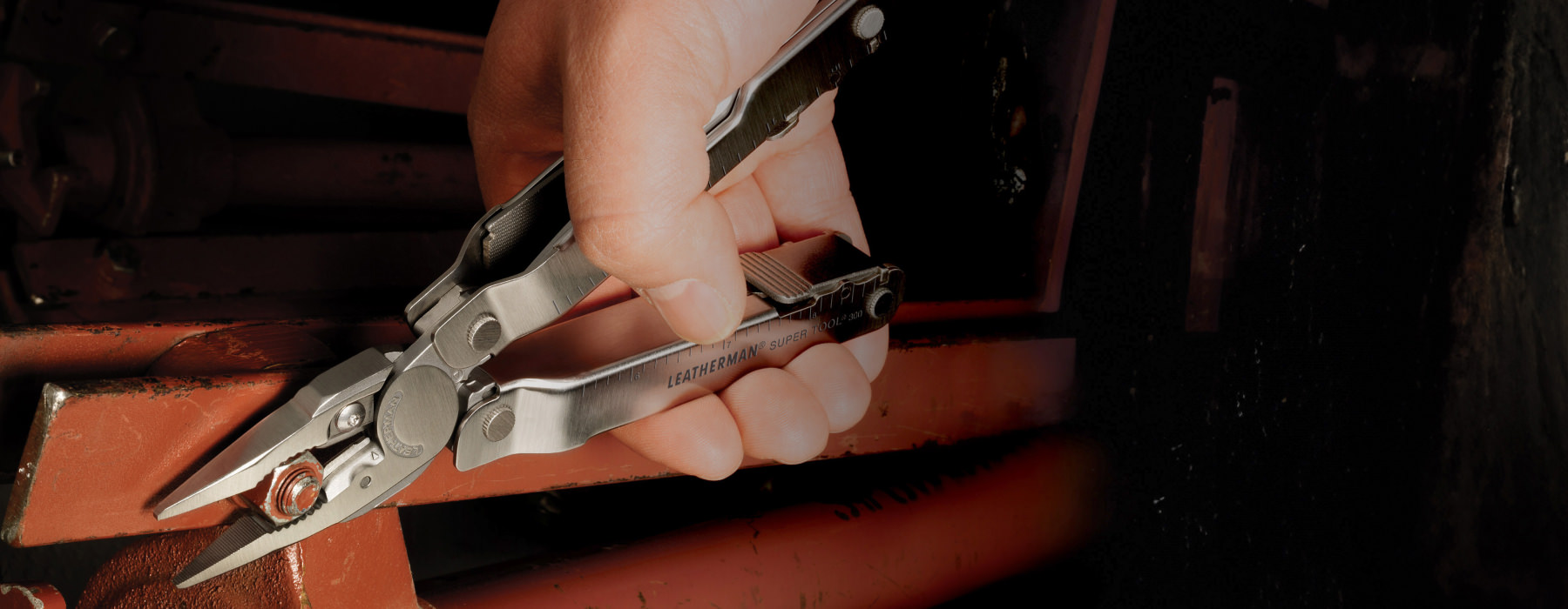 Leatherman Super Tool being used to adjust a bolt on a red machine.