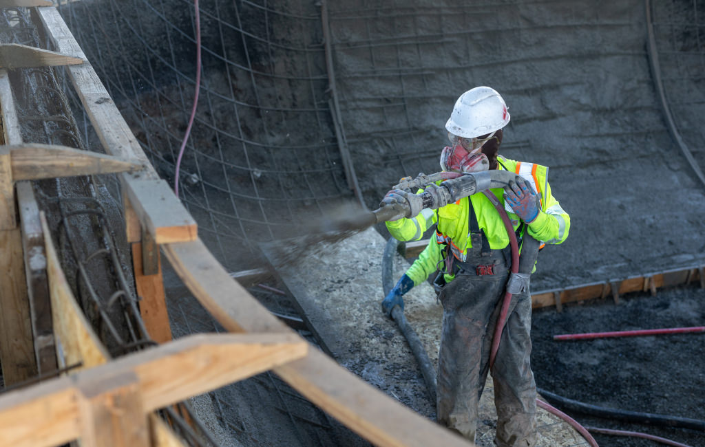 Worker spraying concrete onto a wall with rebar.