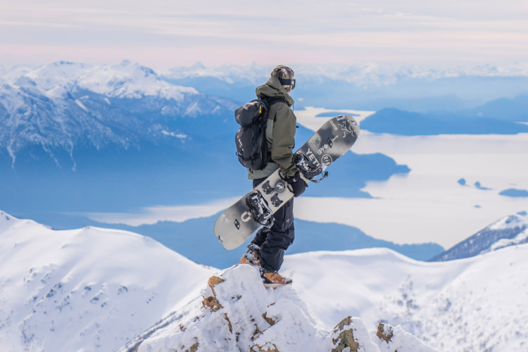 Man with a snowboard on the top of a mountain.