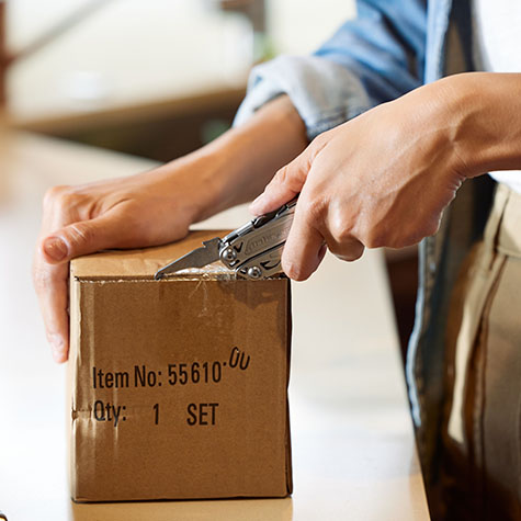 Woman using a Leatherman Wingman package opener tool to open a taped box.