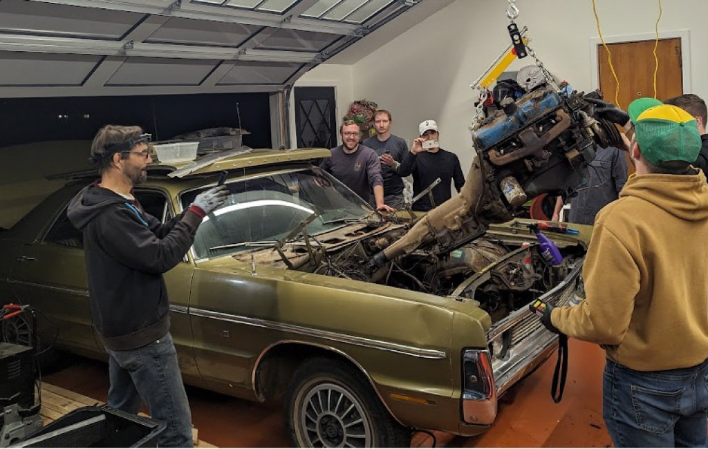 A group of men around a car watching the engine be put in