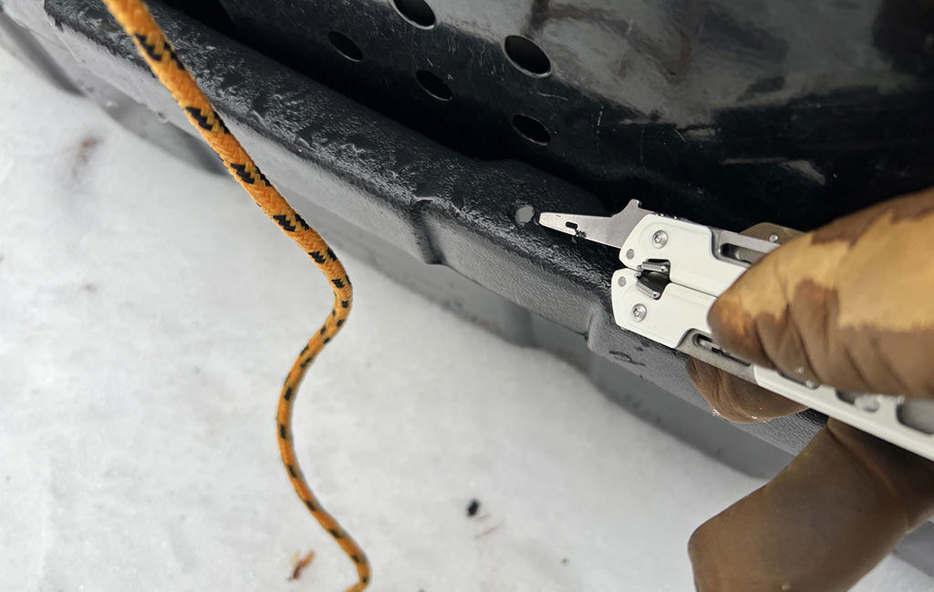 Gloved hand using Leatherman Garage 005 to drill a new tie-down hole into a sled.